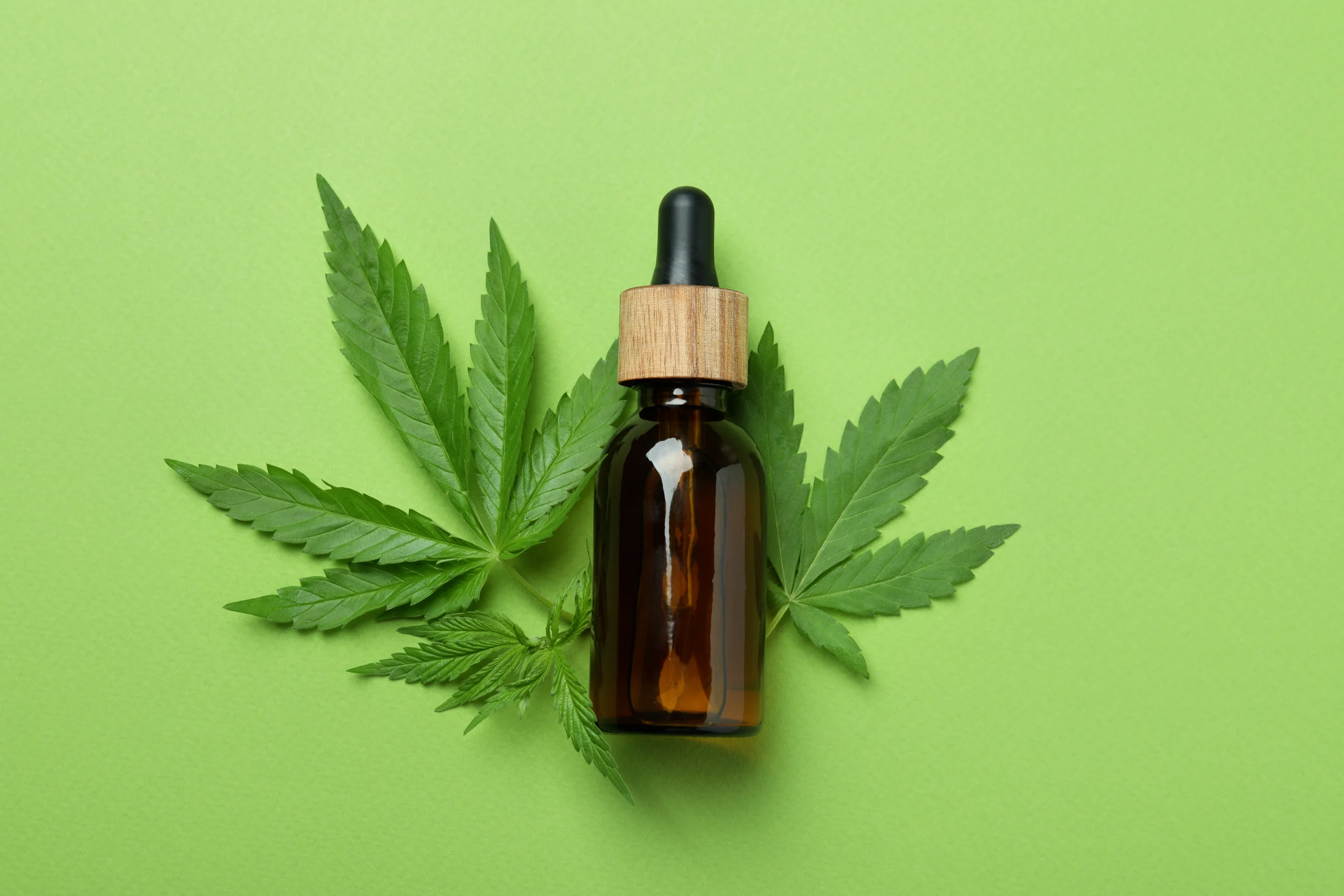 Cannabis oil in front of hemp leaves on a green background; for article "What is Cannabis Lube"